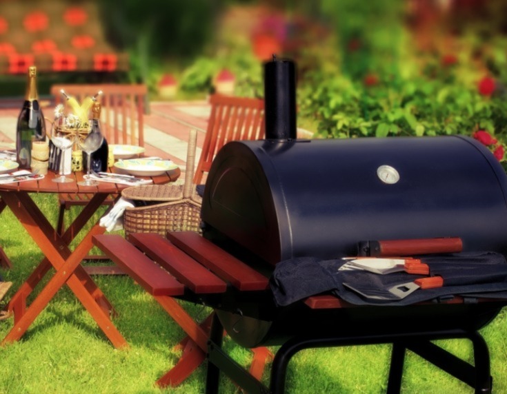 BBQ in the foreground with a garden table behind set with wine glasses and champagne